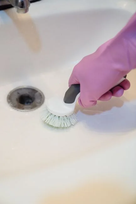 Person using spray bottle and cloth for cleaning a kitchen shelf, ensuring hygiene and cleanliness.